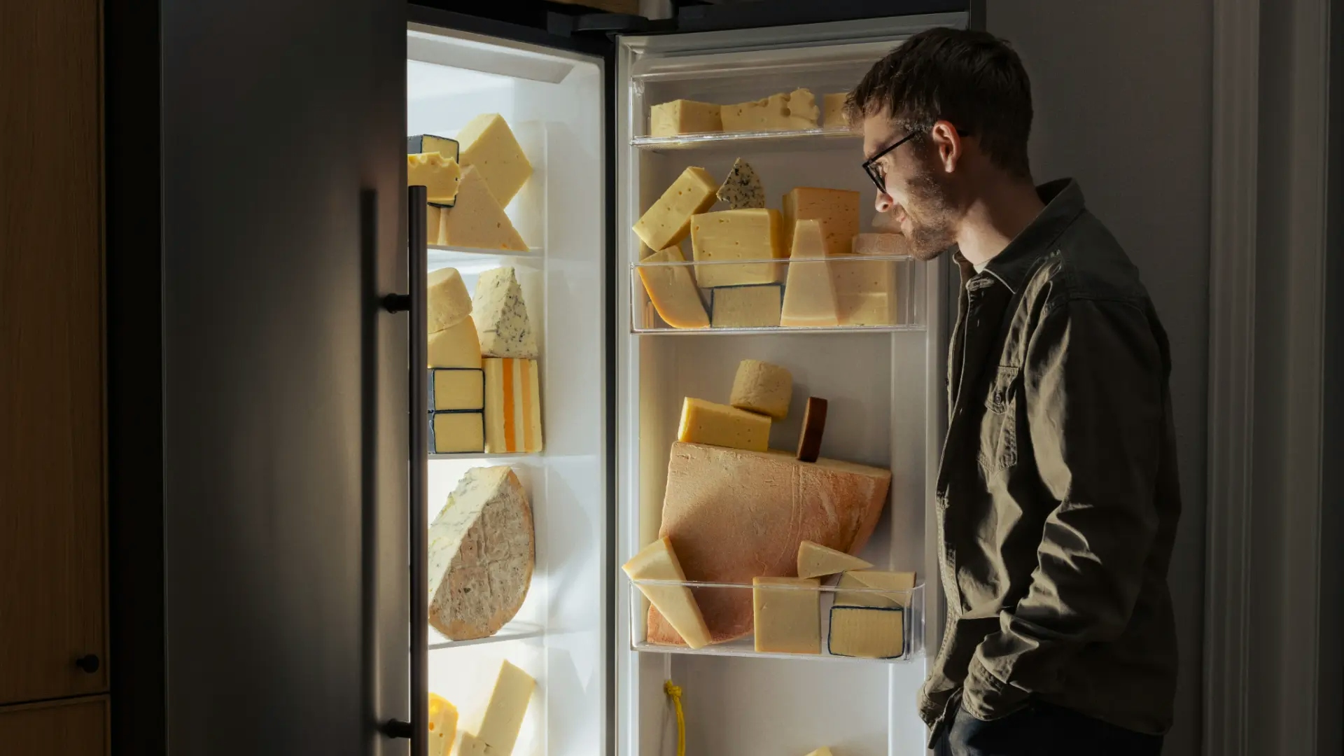 Man som öppnar kylskåp fyllt med ost som lyser upp rummet - Ny Studio